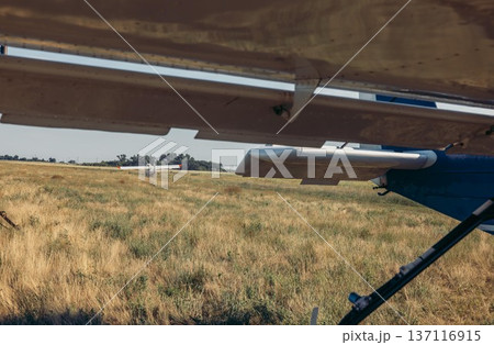 An agricultural airplane prepares for chemical spraying over a golden field. The scene captures the aircraft's wing and the vast landscape below. An agricultural airplane prepares for chemical spraying over a golden field. The scene captures the aircraft's wing and the vast landscape below. 137116915