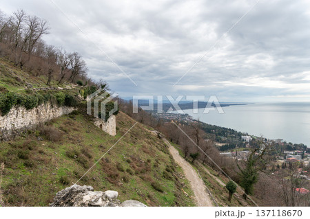 Anacopia fortress walls along hillside overlooking New Athos coastline and Black Sea in Abkhazia under cloudy sky, Historic architecture and coastal landscape suitable for tourism marketing 137118670