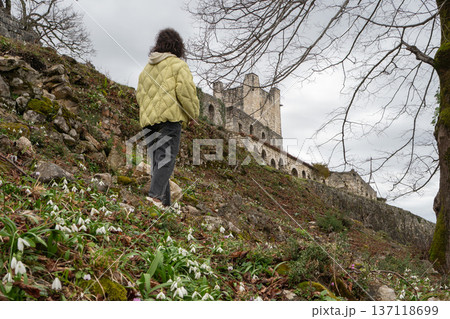 Woman walking uphill among blooming snowdrops toward Anacopia fortress ruins in Abkhazia under cloudy sky, Travel lifestyle scene suitable for tourism marketing, spring season campaigns Woman walking uphill among blooming snowdrops toward Anacopia fortress ruins in Abkhazia under cloudy sky, Travel lifestyle scene suitable for tourism marketing, spring season campaigns 137118699
