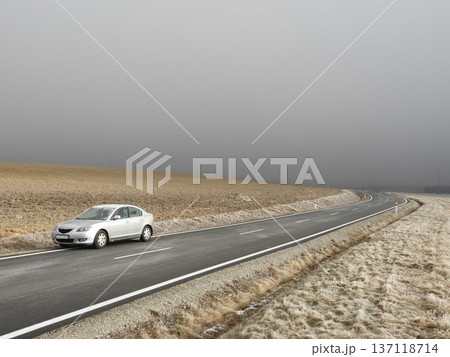 Silver car parked on a winding rural asphalt road through frosty farmland under dense winter fog, Silver car parked on a winding rural asphalt road through frosty farmland under dense winter fog, 137118714