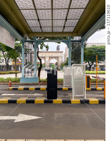 Jakarta, Indonesia - February 08 2026: Automatic entrance gate with parking barriers and ticket machines in front of a grand Asia arch with horse statues on top. 137119610
