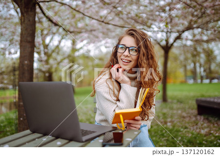 Beautiful female student is using laptop, notepad to prepare for outdoor classes. Education concept. 137120162