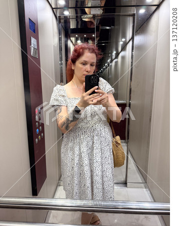 Woman in white dress taking selfie in elevator mirror with round straw bag. Fashion, summer style, and lifestyle identity Woman in white dress taking selfie in elevator mirror with round straw bag. Fashion, summer style, and lifestyle identity 137120208