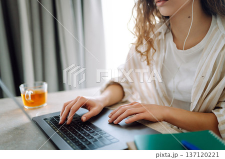 Hands of a young woman in headphones typing on the keyboard of a modern laptop at home, on the floor Hands of a young woman in headphones typing on the keyboard of a modern laptop at home, on the floor 137120221