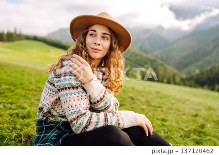 Stylish female traveler in hat has fun on top of hill, enjoys mountain landscape. Active lifestyle. 137120462