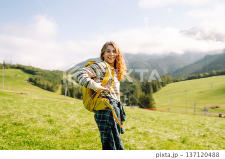 Female tourist with yellow backpack on top of mountain enjoying view of valley. Hiking concept. 137120488