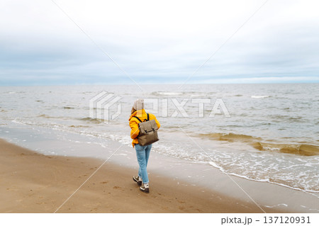 Woman tourist in a yellow jacket posing by the sea. Travelling, lifestyle, adventure. 137120931