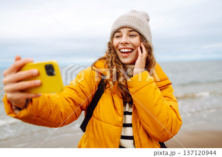 Portrait of young tourist in yellow jacket with phone in hands on seashore. Travel concept, blogging Portrait of young tourist in yellow jacket with phone in hands on seashore. Travel concept, blogging 137120944