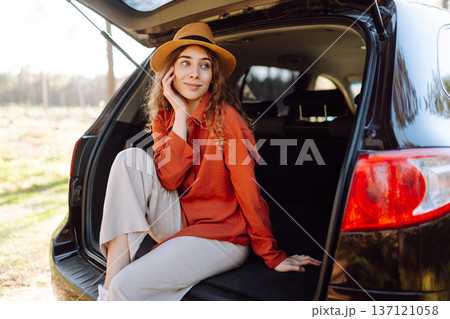 Happy woman enjoying nature while sitting in the trunk of her car during a solo trip. Road trip Happy woman enjoying nature while sitting in the trunk of her car during a solo trip. Road trip 137121058