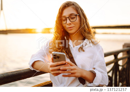 Young woman uses phone walk on embankment. Concept of vacation, technology, weekend. Young woman uses phone walk on embankment. Concept of vacation, technology, weekend. 137121257