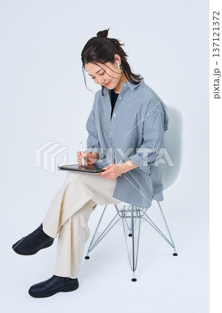カジュアルな服装でタブレットPCを使う若い女性 カジュアルな服装でタブレットPCを使う若い女性 137121372