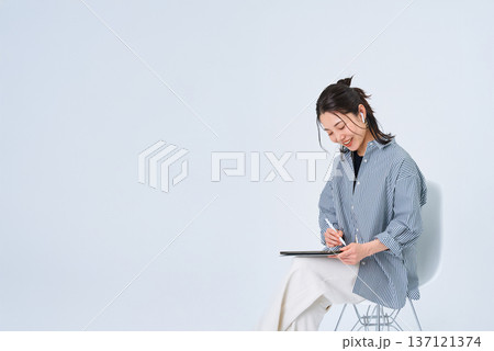 カジュアルな服装でタブレットPCを使う若い女性 カジュアルな服装でタブレットPCを使う若い女性 137121374