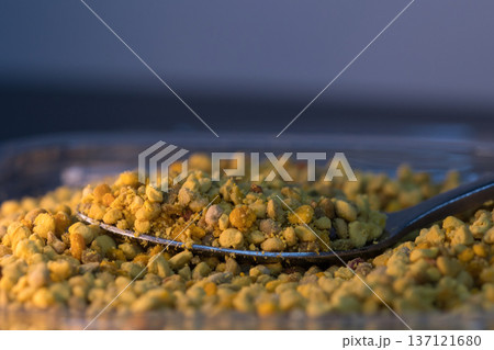 Close-up of natural bee pollen granules in vibrant yellow and orange tones, showcasing their organic texture.  137121680
