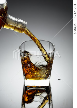 The amber-gold strong alcoholic beverage is poured into a glass. The amber-gold strong alcoholic beverage is poured into a glass. 137121701