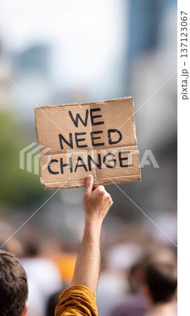 Protester raises a homemade cardboard sign with the inscription we need change during a political demonstration, expressing the collective desire for societal transformation 137123067