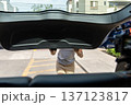 A teenager is standing in front of a car with a black trunk 137123817