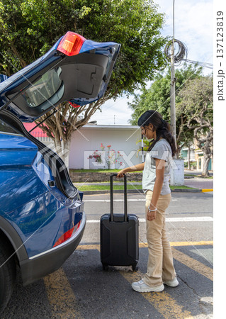A teenager is standing next to a blue car with a suitcase in the trunk A teenager is standing next to a blue car with a suitcase in the trunk 137123819
