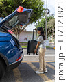 A teenager is pulling a suitcase out of the back of a blue car 137123821