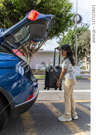 A teenager is pulling a suitcase out of the back of a blue car 137123821