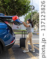 A teenager is pulling a suitcase out of the back of a blue car 137123826