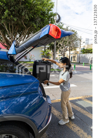 A teenager is opening the trunk of a blue car A teenager is opening the trunk of a blue car 137123830
