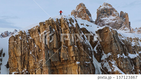 Ski mountaineer crossing a snowy ridge in the Dolomites with dramatic alpine peaks and blue sky in the background, capturing winter adventure and breathtaking mountain landscape. 137123867