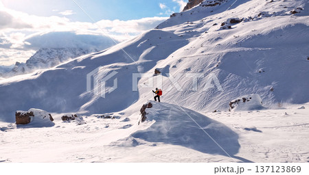 Ski mountaineer standing on a snowy rock in the Dolomites with wind blowing snow across alpine slopes, capturing winter adventure, solitude and dramatic mountain landscape. 137123869