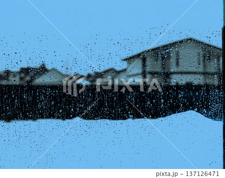 Raindrops on window glass with blurred suburban houses background. Moody rainy day atmosphere in a residential area. Water droplets on glass texture, blue tones, concept of solitude and cozy home. Raindrops on window glass with blurred suburban houses background. Moody rainy day atmosphere in a residential area. Water droplets on glass texture, blue tones, concept of solitude and cozy home. 137126471