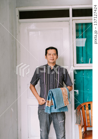 Devoted Man Holding a Traditional Prayer Mat Indoors Devoted Man Holding a Traditional Prayer Mat Indoors 137127424