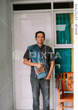Asian Man Holding Prayer Mat at Home Entrance 137127426