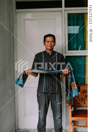 Smiling man proudly holds traditional prayer mat in a home setting 137127431