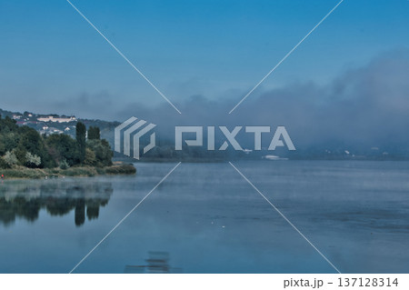 Foggy Lake Landscape with Distant Shoreline and Calm Water 137128314