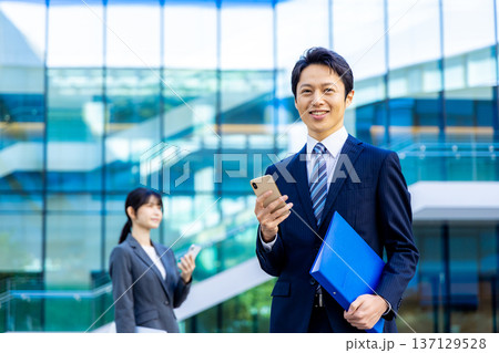 ビジネスマン若い男性、高層ビル、スマホ、ビジネスイメージ ビジネスマン若い男性、高層ビル、スマホ、ビジネスイメージ 137129528