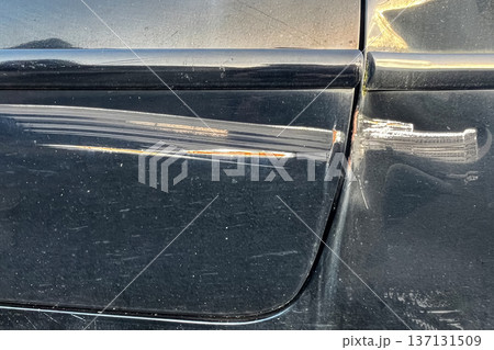 Scratched black car door with rust marks and damaged paint surface close up showing vehicle body detail and wear. 137131509