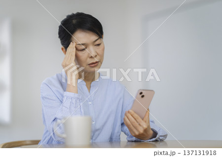 スマートフォンを見ながら考え込む50代後半の女性 137131918