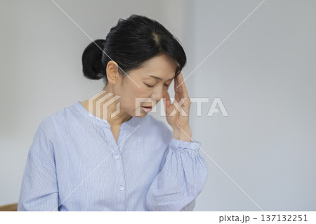 こめかみをおさえてうつむく50代後半の女性 137132251