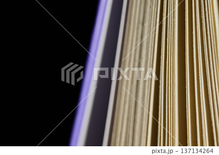 Extreme close-up of paper edges in an open book against a dark background with blue light accents 137134264