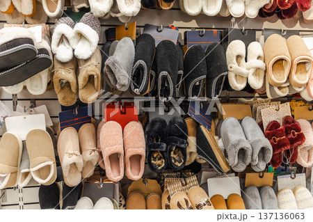 Assortment of cozy home slippers displayed on retail store wall, warm indoor footwear collection arranged in clothing shop interior Assortment of cozy home slippers displayed on retail store wall, warm indoor footwear collection arranged in clothing shop interior 137136063