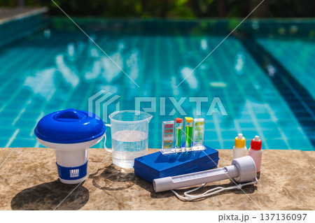 Liquid pool chemicals poured into swimming pool water using a transparent measuring cup with volume markings 137136097