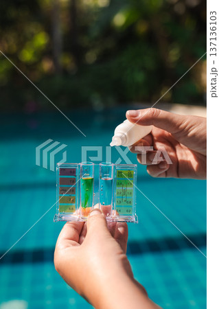 Hand holding pool water test kit measuring pH level and chlorine concentration in swimming pool during routine maintenance and water quality control 137136103