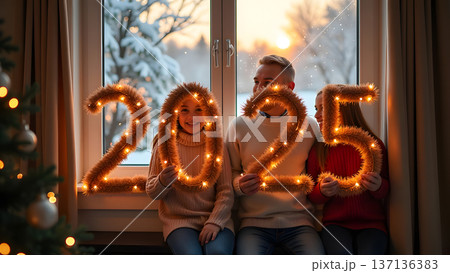 In a cozy room, the family poses by a big window showcasing a snowy view. Each member holds part of a luminous 2025 garland, celebrating the festive season 137136383