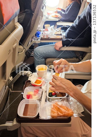 Economy class passengers enjoying meal served in flight in a cramped space with small leg room. Economy class passengers enjoying meal served in flight in a cramped space with small leg room. 137136532