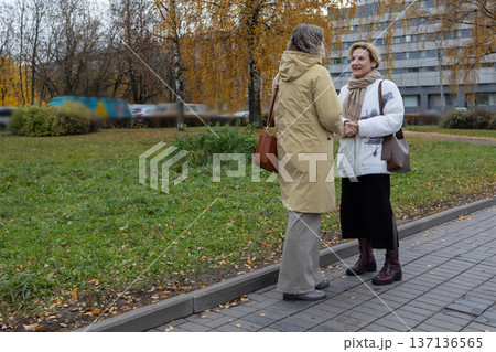 Connection. Female friends meeting outdoors in urban environment smiling and preparing to hug beside street with passing traffic and trees. 137136565