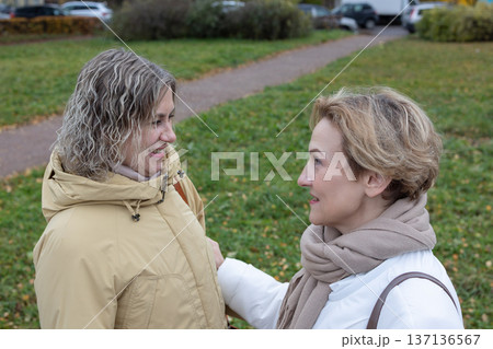 Reunion. Two mature women approaching each other with open arms on city sidewalk near road expressing joy during autumn day. 137136567