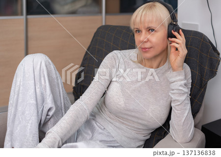 Woman sitting in armchair at home listening music through black over ear headphones calm indoor lifestyle leisure concept. Woman sitting in armchair at home listening music through black over ear headphones calm indoor lifestyle leisure concept. 137136838