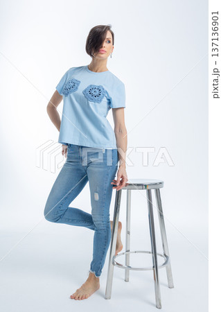 Beautiful woman of model appearance. Girl in blue clothes on grey background. Pretty female with trendy makeup posing in studio. Vertical photo. High quality photo 137136901