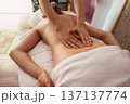 Close-up of a spa therapist hands gliding over a young woman bare back during relaxing massage, warm soft light highlighting smooth skin, cozy treatment room and tranquil wellness atmosphere. 137137774