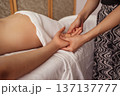 Close-up of spa therapist gently massaging a woman hand as she lies under a white sheet, warm light on skin and soft textiles creating a calm, nurturing wellness atmosphere 137137777