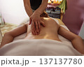 Close-up of a spa therapist hands gliding over a young woman bare back during relaxing massage, warm soft light highlighting smooth skin, cozy treatment room and tranquil wellness atmosphere. 137137780