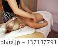 Close-up view of professional massage therapist performing back massage on a blonde woman lying on table, in spa room with warm light, calm tones, and relaxing atmosphere. 137137791